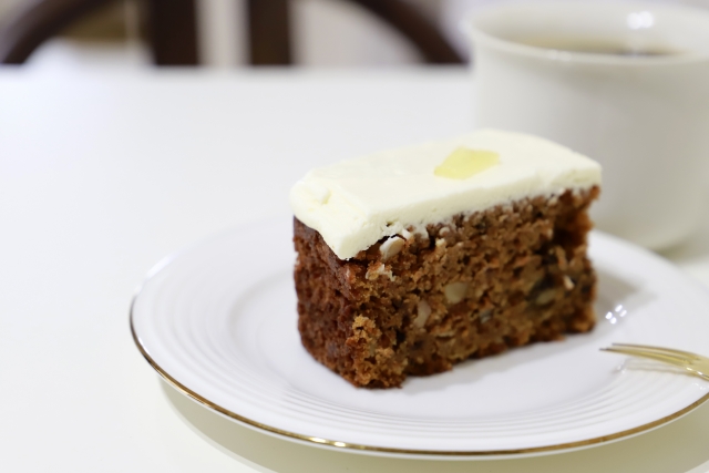 白いクリームをのせたキャロットケーキとカップ